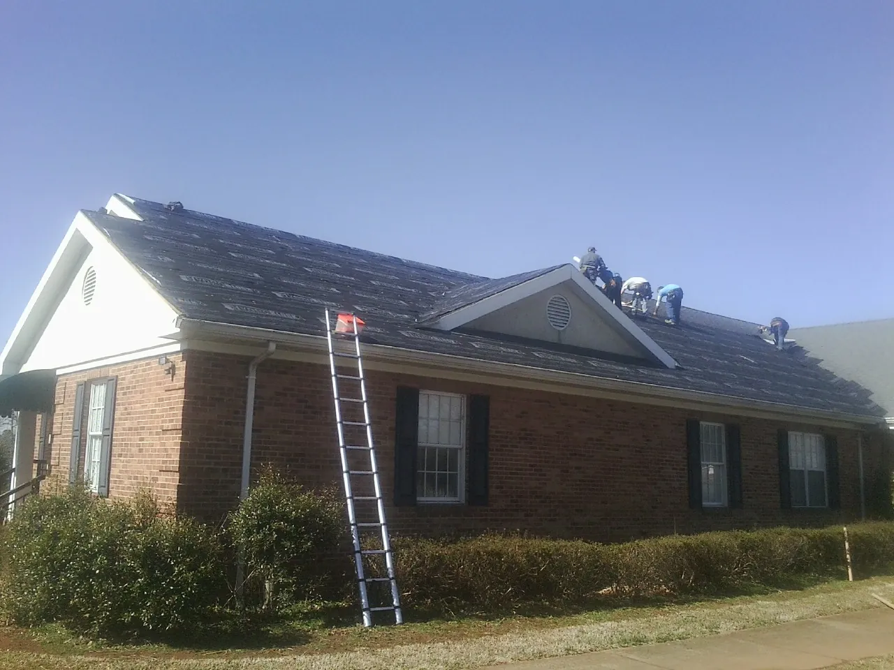 Crew tearing shingles off a brick ranch roof with a ladder set — Metal Roof Repair work by our crew in Willow Hill