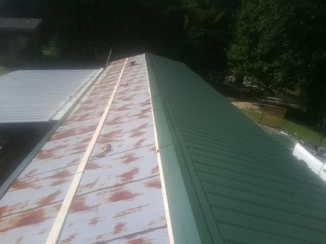 Old rusted panels beside newly installed green metal roofing in Willow Hill
