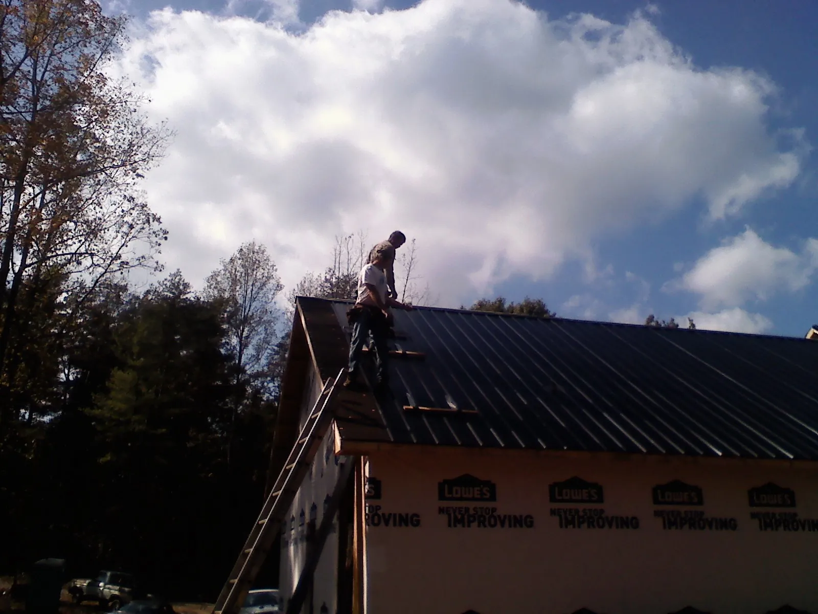 Roofer fastening dark metal panels high against a cloudy sky, from a Roof Inspection job in Willow Hill