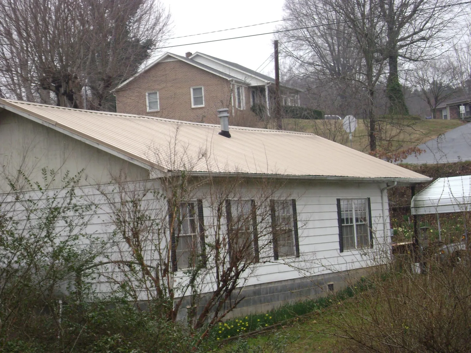 Tan metal roof on a white sided house set into a hillside — Commercial Roofing by Roofing Brothers in Willow Hill